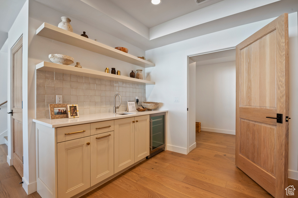 Bar with beverage cooler, baseboards, backsplash, light wood-style floors, and a sink