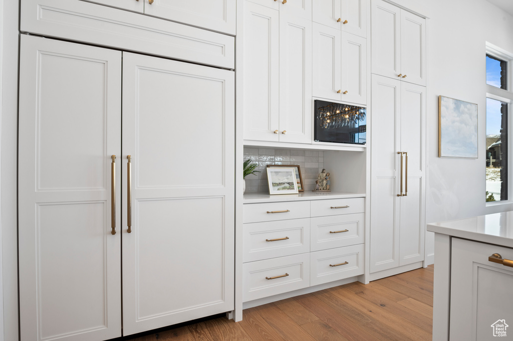 Kitchen featuring white cabinets, light wood-style floors, tasteful backsplash, and light countertops