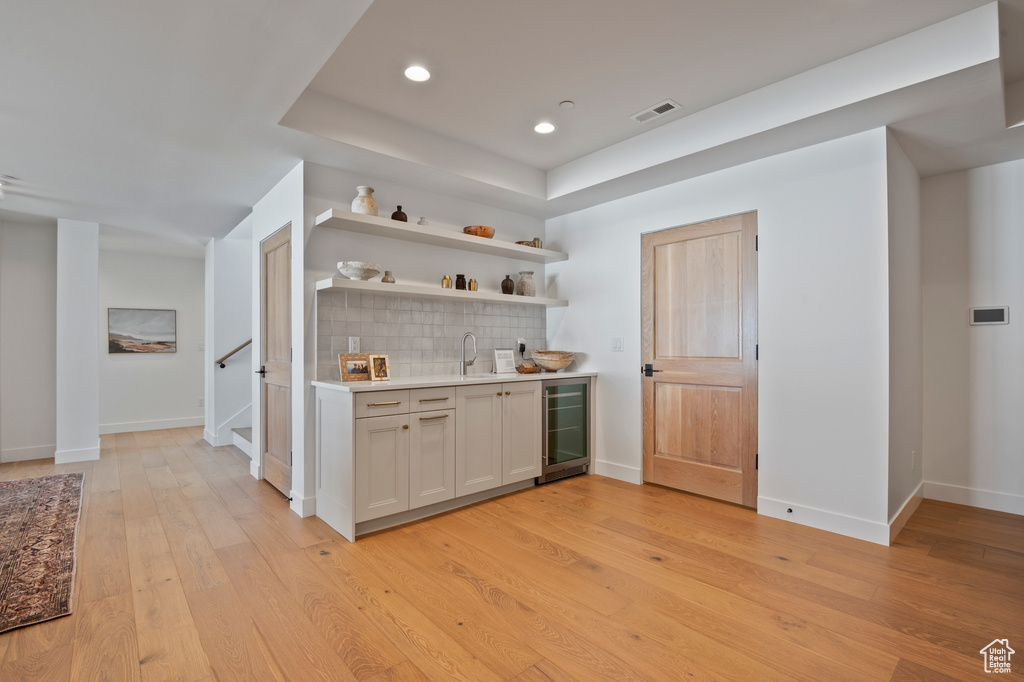 Bar featuring wine cooler, light wood-style flooring, a sink, visible vents, and tasteful backsplash