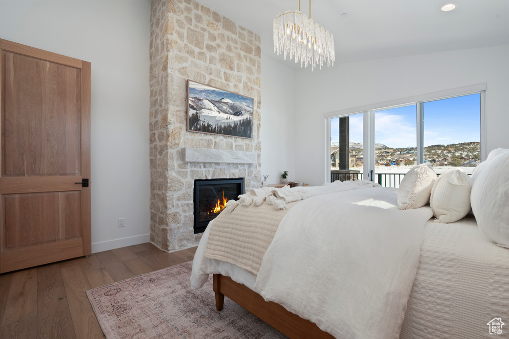 Bedroom with a stone fireplace, baseboards, access to exterior, light wood-type flooring, and an inviting chandelier