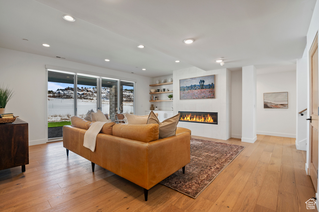 Living room with light wood-type flooring, recessed lighting, and a glass covered fireplace