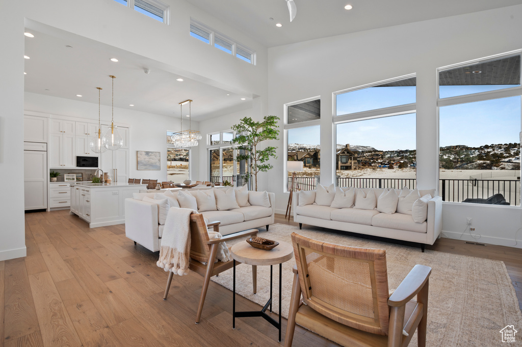 Living room featuring light wood finished floors, recessed lighting, a high ceiling, an inviting chandelier, and baseboards