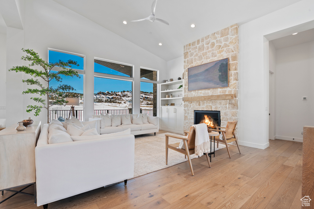 Living area featuring a ceiling fan, light wood-style flooring, a stone fireplace, high vaulted ceiling, and recessed lighting