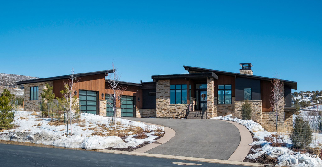 Modern home with a garage, stone siding, aphalt driveway, and a chimney