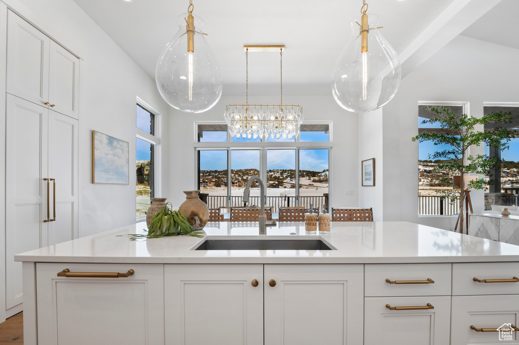 Kitchen featuring white cabinetry, light countertops, a sink, and pendant lighting