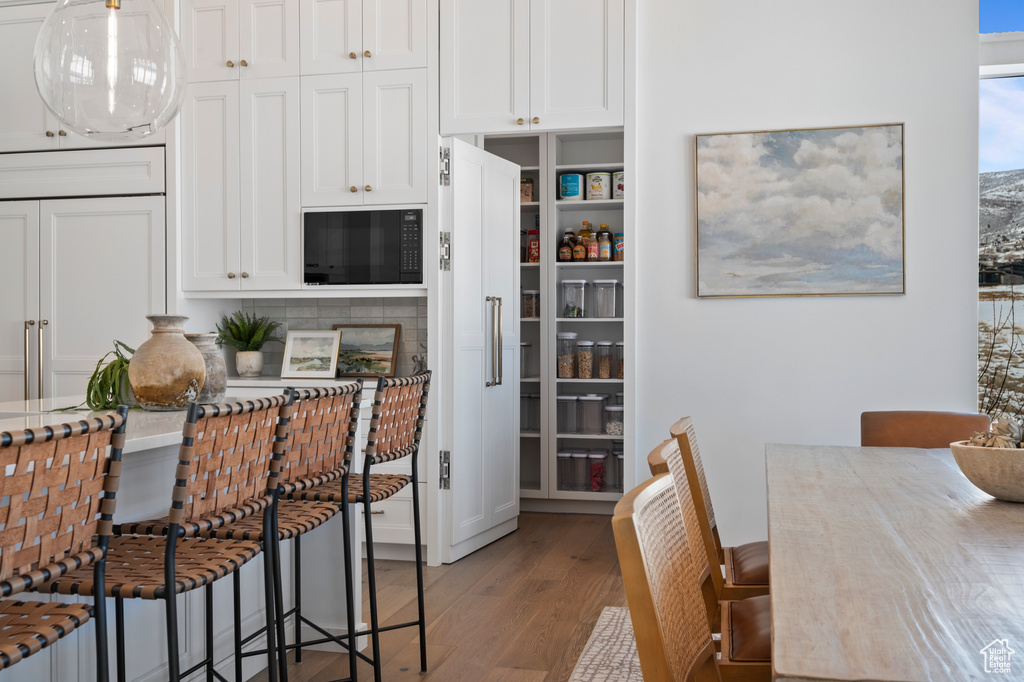 Kitchen with black microwave, light wood-type flooring, white cabinetry, and decorative light fixtures