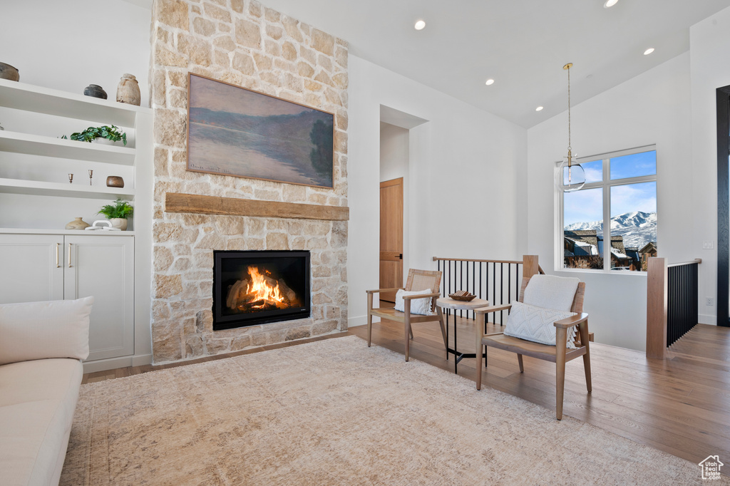 Living room with high vaulted ceiling, a stone fireplace, wood finished floors, and recessed lighting