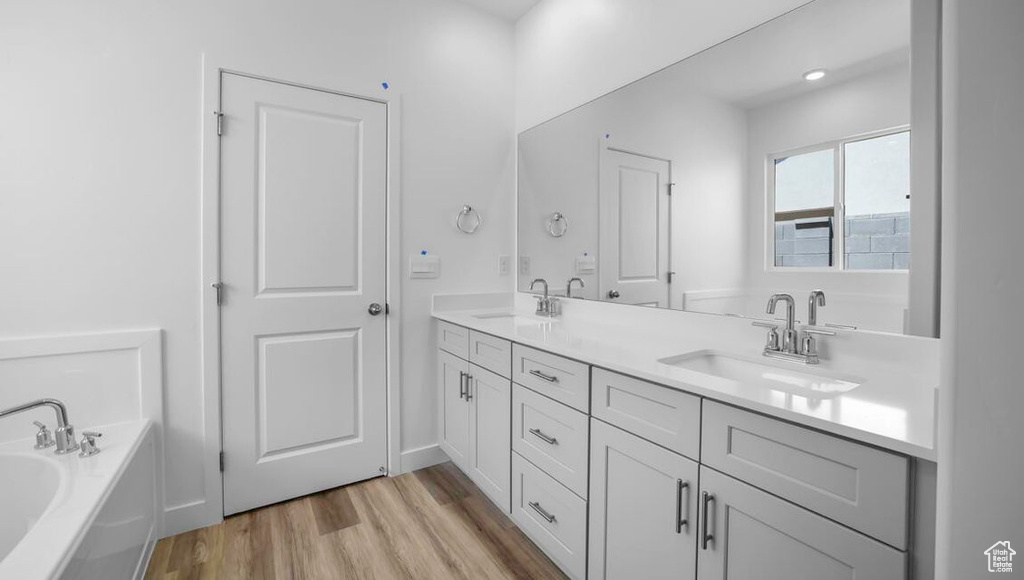 Bathroom featuring double vanity, a sink, a bath, and wood finished floors