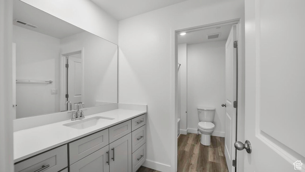 Full bath with baseboards, visible vents, toilet, wood finished floors, and vanity