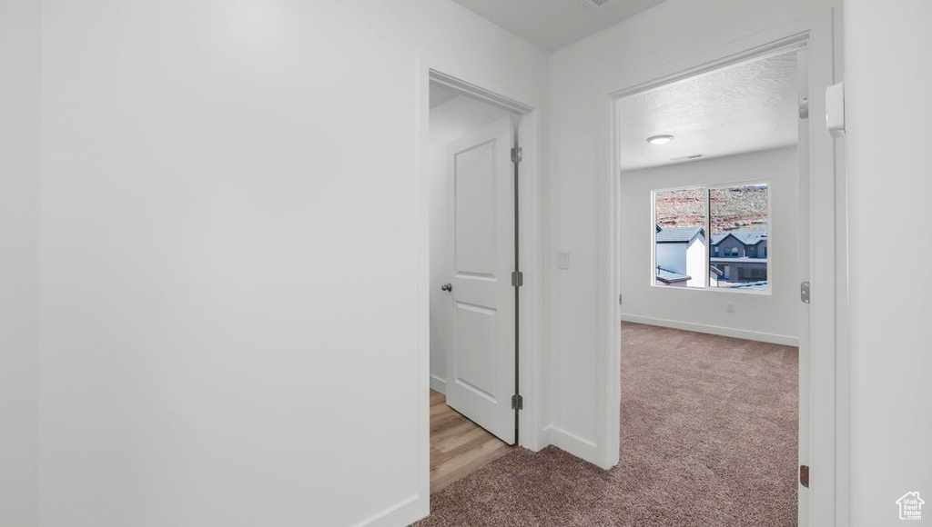 Hall featuring light carpet, a textured ceiling, and baseboards