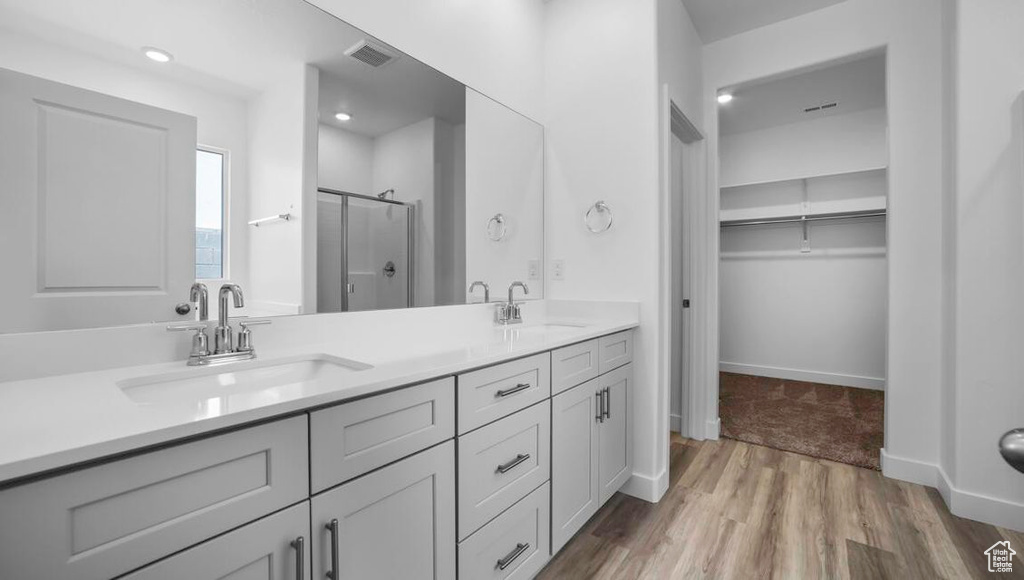Bathroom with double vanity, visible vents, a sink, a shower stall, and wood finished floors