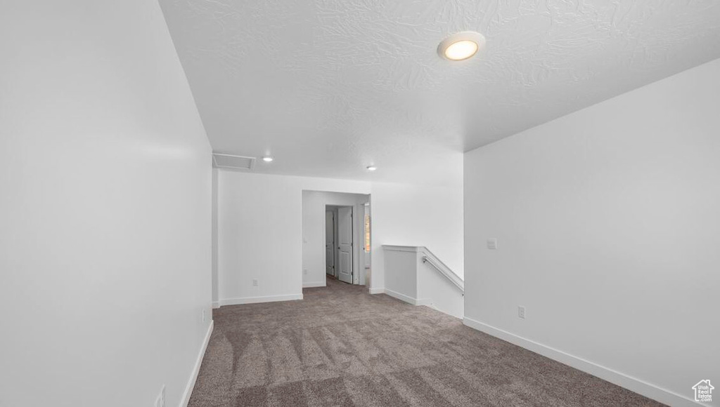Empty room featuring a textured ceiling, carpet flooring, and baseboards