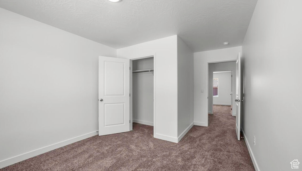 Unfurnished bedroom with a textured ceiling, baseboards, dark colored carpet, and a closet