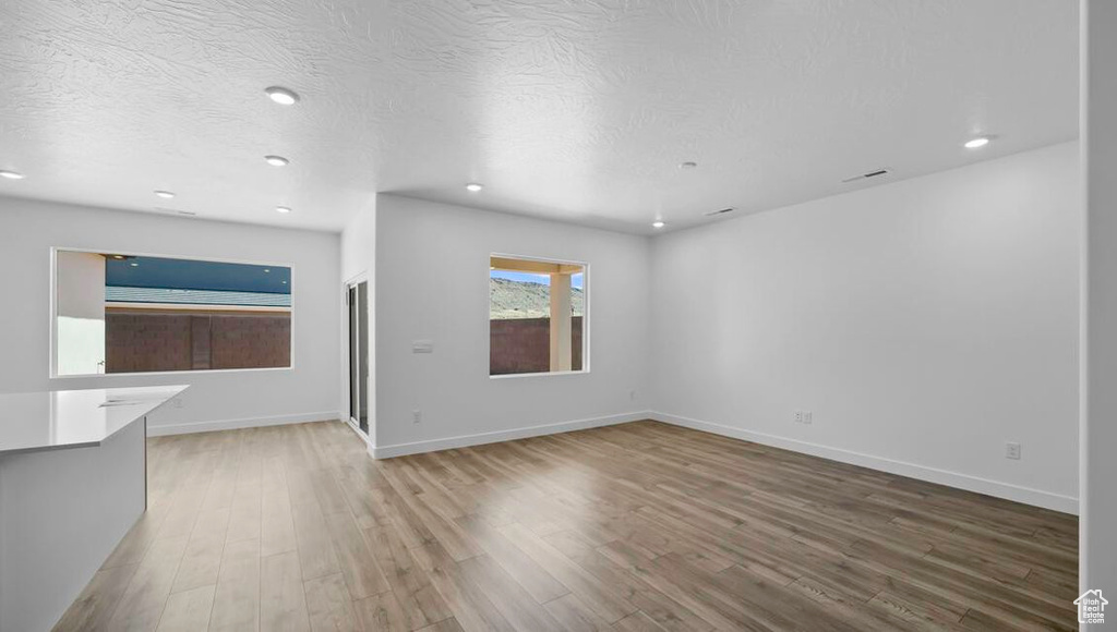 Unfurnished living room featuring a textured ceiling, recessed lighting, wood finished floors, and baseboards
