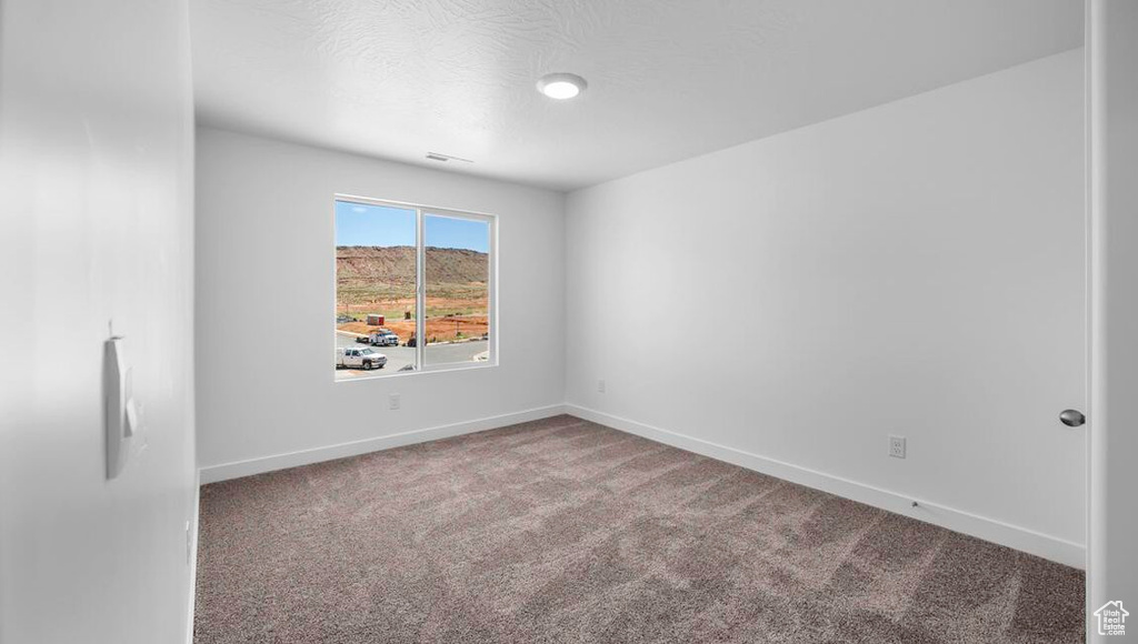 Empty room with a textured ceiling, carpet, and baseboards