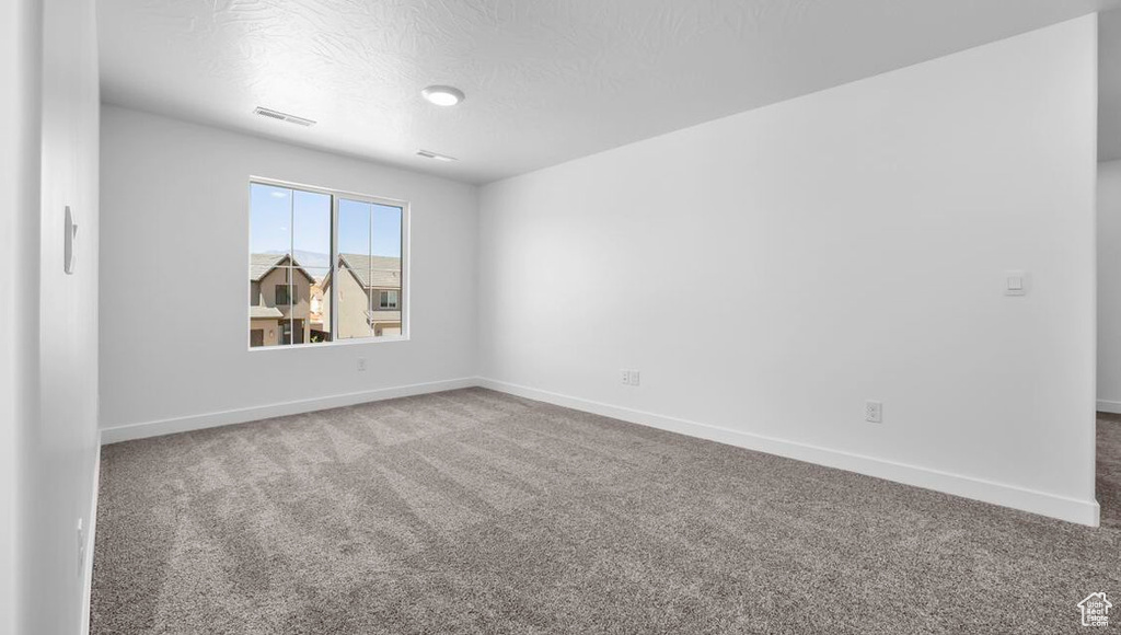 Carpeted spare room featuring visible vents, a textured ceiling, and baseboards