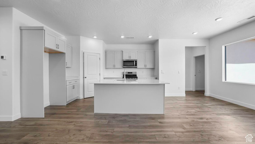 Kitchen featuring a kitchen island with sink, recessed lighting, stainless steel appliances, light countertops, and dark wood-style floors