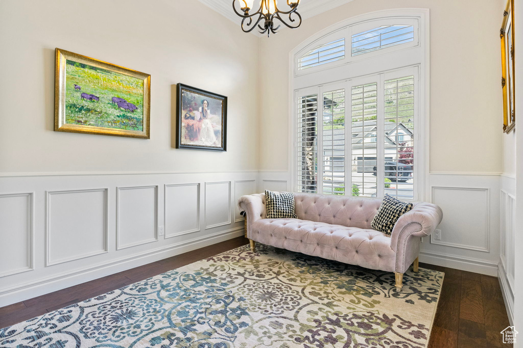 Living area with a decorative wall, dark wood-type flooring, ornamental molding, wainscoting, and a chandelier