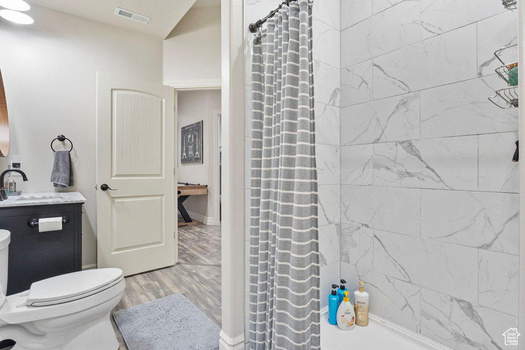 Full bathroom with toilet, wood finished floors, vanity, visible vents, and a shower with curtain
