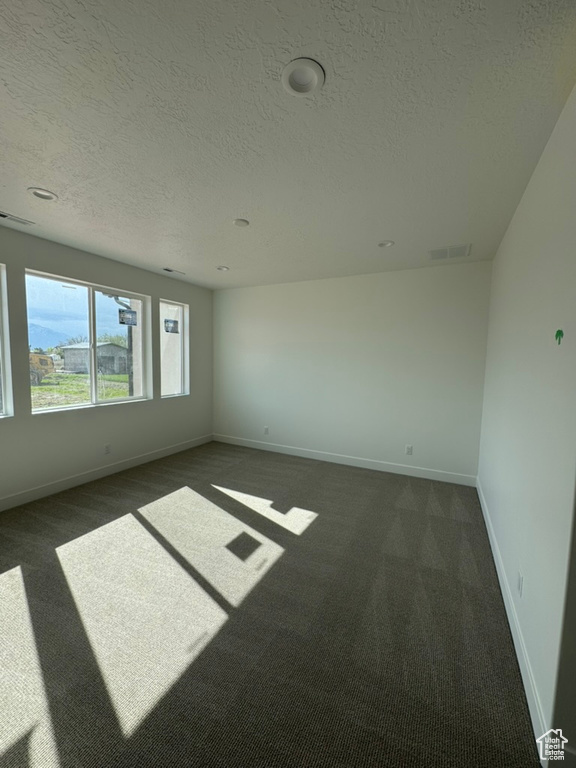 Empty room with dark carpet, a textured ceiling, visible vents, and baseboards