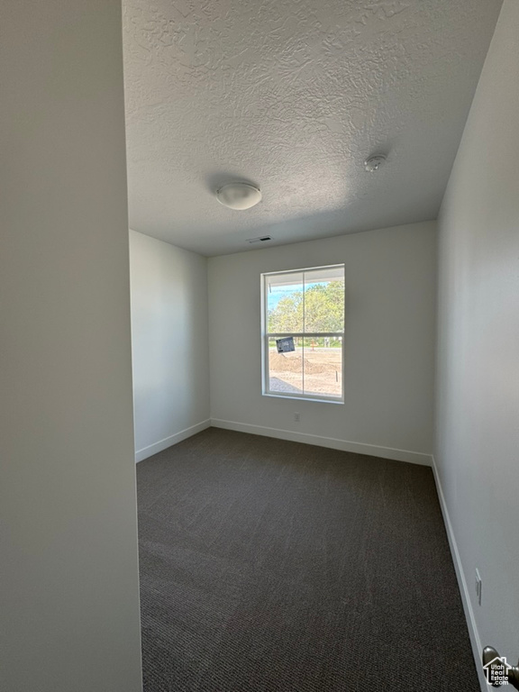 Spare room featuring dark colored carpet, a textured ceiling, and baseboards