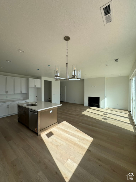 Kitchen featuring stainless steel dishwasher, visible vents, an inviting chandelier, wood finished floors, and an island with sink