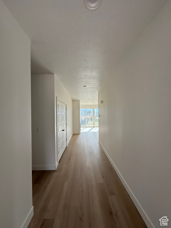 Hallway with baseboards, wood finished floors, and a textured ceiling