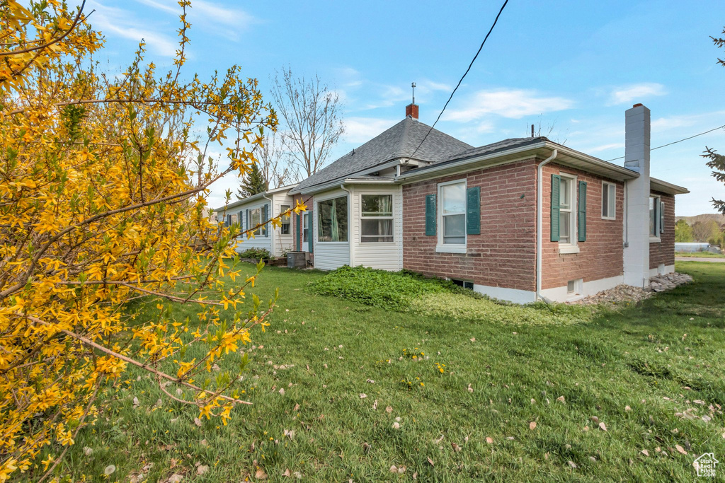 View of property exterior with a lawn, a chimney, and brick siding