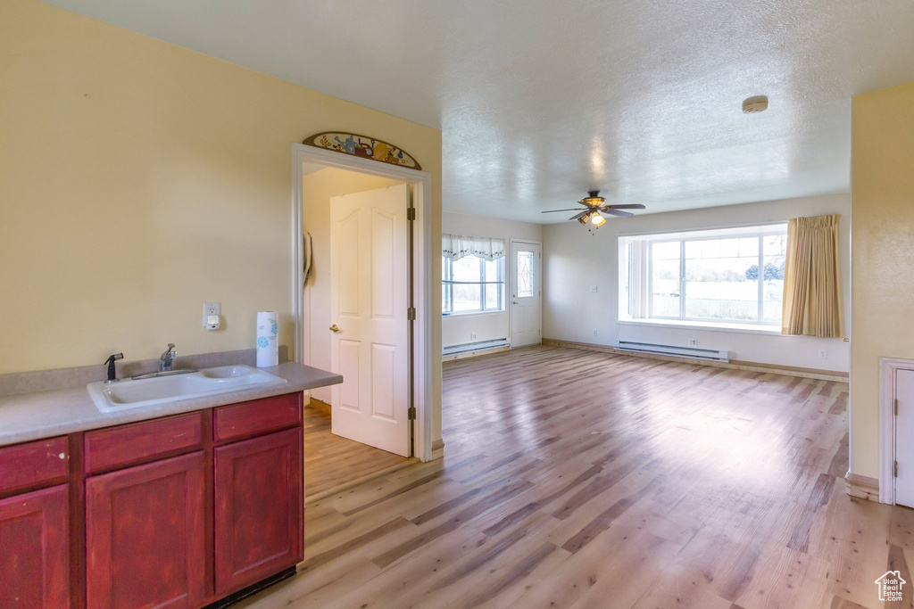 Kitchen with a ceiling fan, dark brown cabinets, a baseboard radiator, a sink, and light wood finished floors