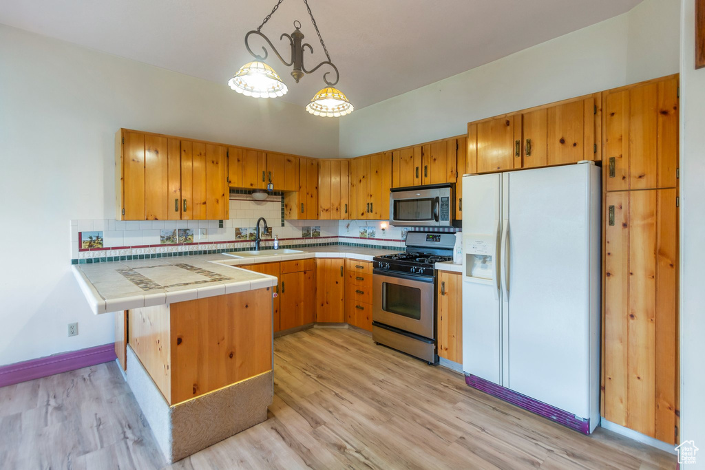 Kitchen featuring tile counters, tasteful backsplash, a sink, light wood finished floors, and appliances with stainless steel finishes
