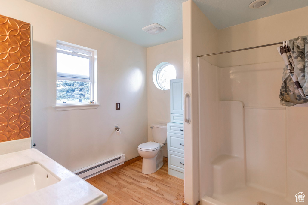 Full bath featuring a shower, a baseboard heating unit, toilet, and wood finished floors