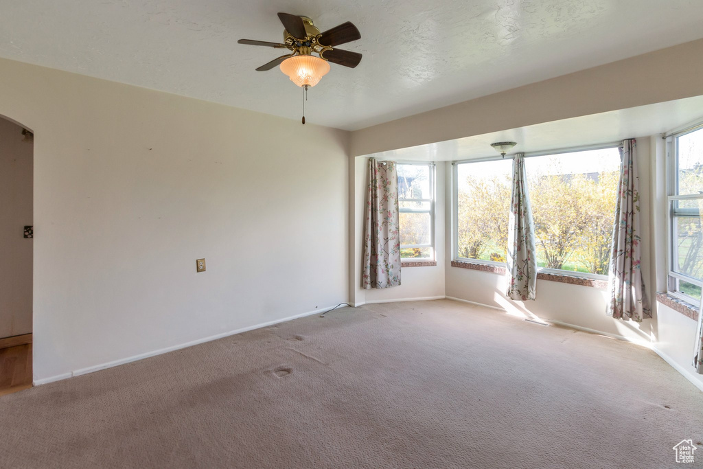 Carpeted empty room featuring arched walkways, baseboards, and a ceiling fan