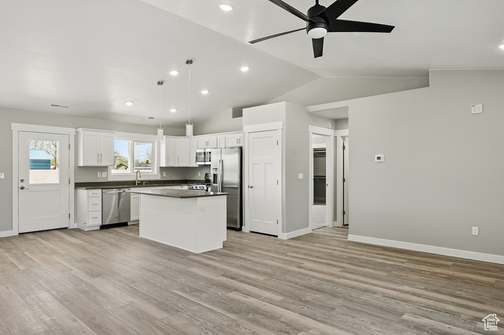 Kitchen featuring a ceiling fan, dark countertops, a center island, a sink, and stainless steel appliances