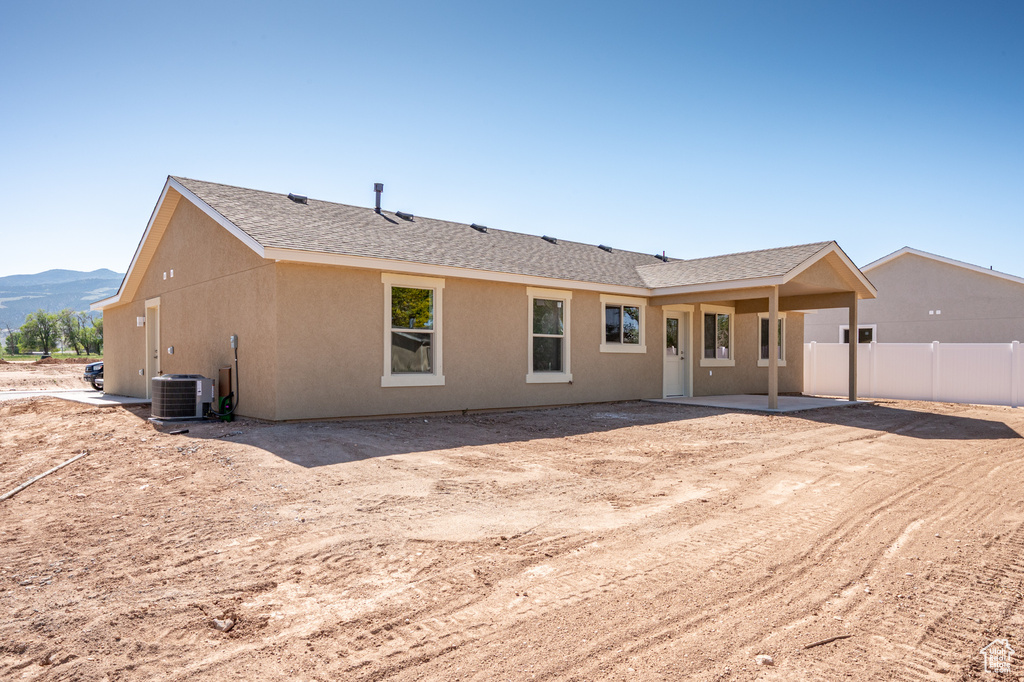 Rear view of house featuring a patio area, a mountain view, roof with shingles, stucco siding, and central AC unit