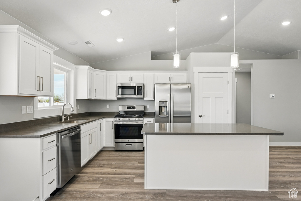 Kitchen with dark countertops, a sink, white cabinets, lofted ceiling, and stainless steel appliances