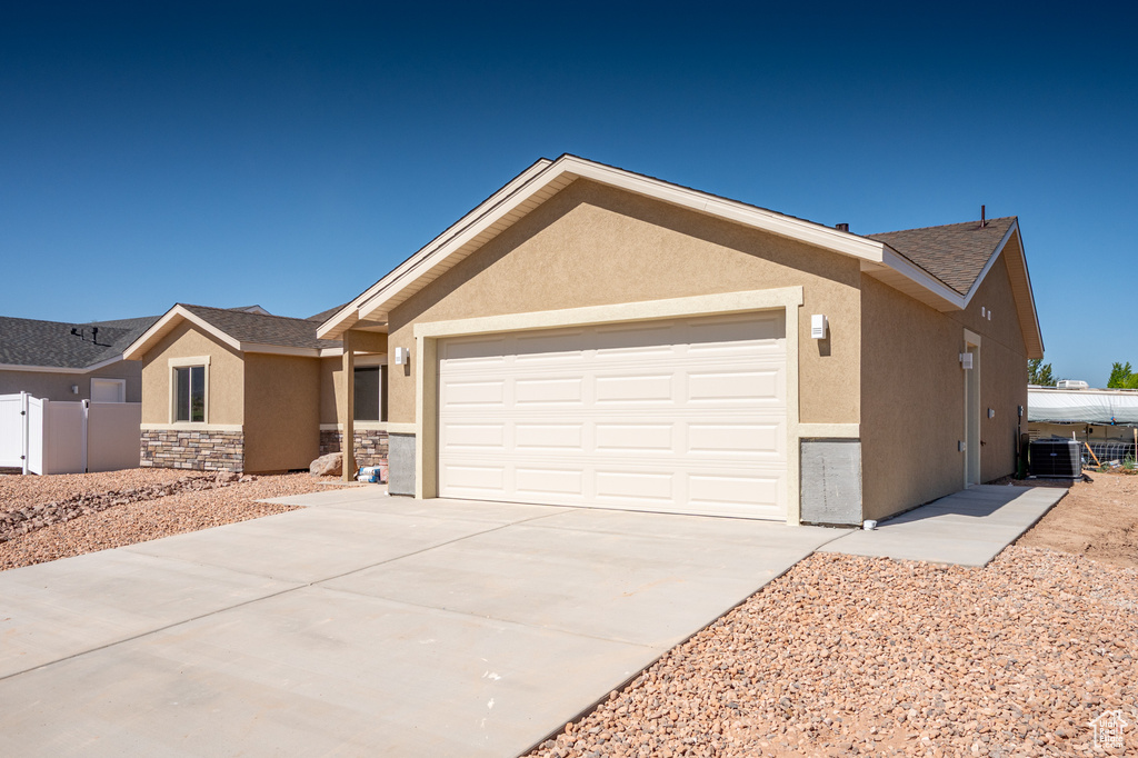 Ranch-style home featuring stucco siding, a garage, stone siding, driveway, and cooling unit