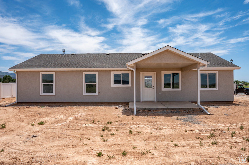 Rear view of house featuring roof with shingles, a patio, and stucco siding