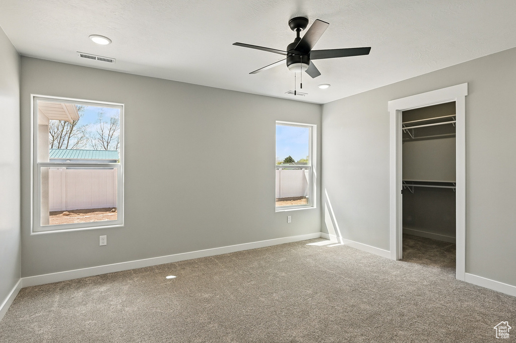 Unfurnished bedroom featuring a spacious closet, multiple windows, carpet flooring, and visible vents