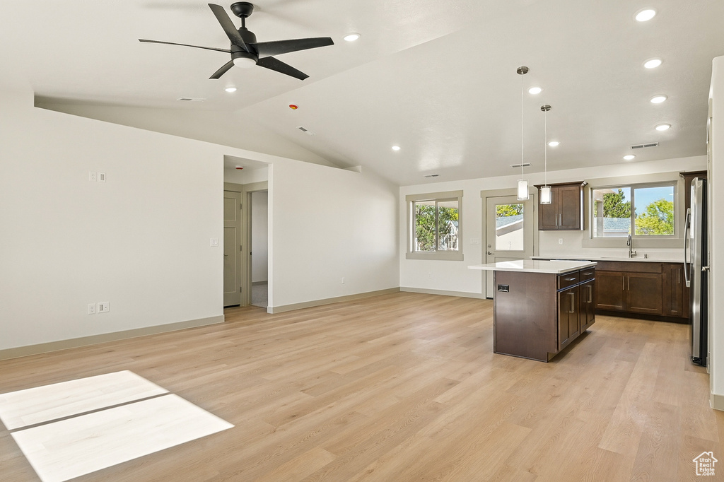 Kitchen with freestanding refrigerator, a center island, dark brown cabinetry, light countertops, and plenty of natural light