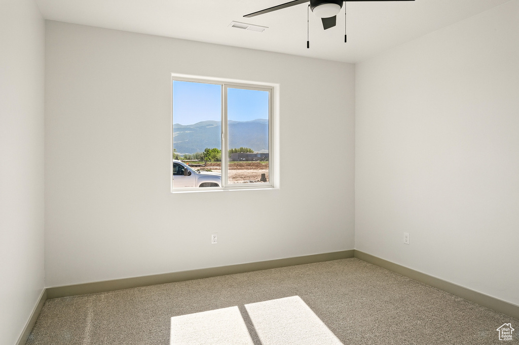 Carpeted spare room featuring a mountain view, a ceiling fan, and baseboards