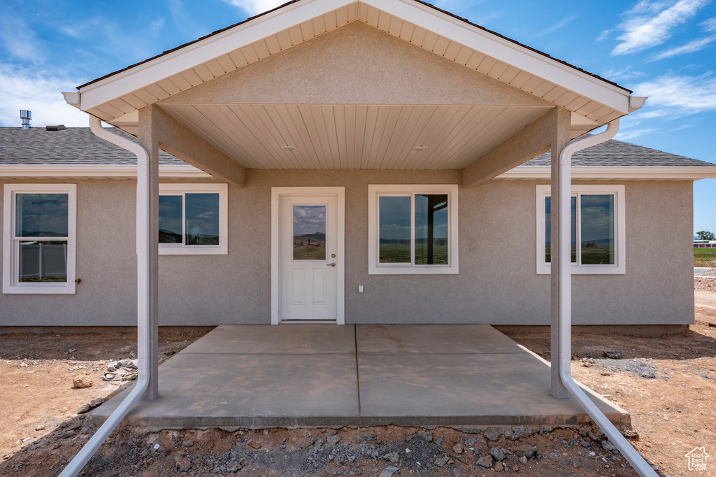 View of exterior entry with a patio, a shingled roof, and stucco siding