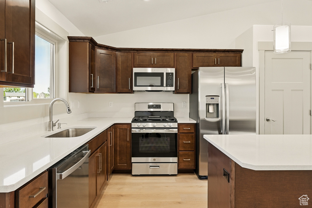 Kitchen with stainless steel appliances, a sink, lofted ceiling, light wood-style floors, and dark brown cabinets