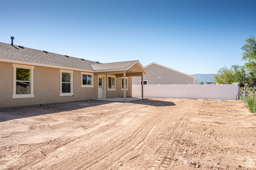 Rear view of house with a shingled roof, a patio, and stucco siding