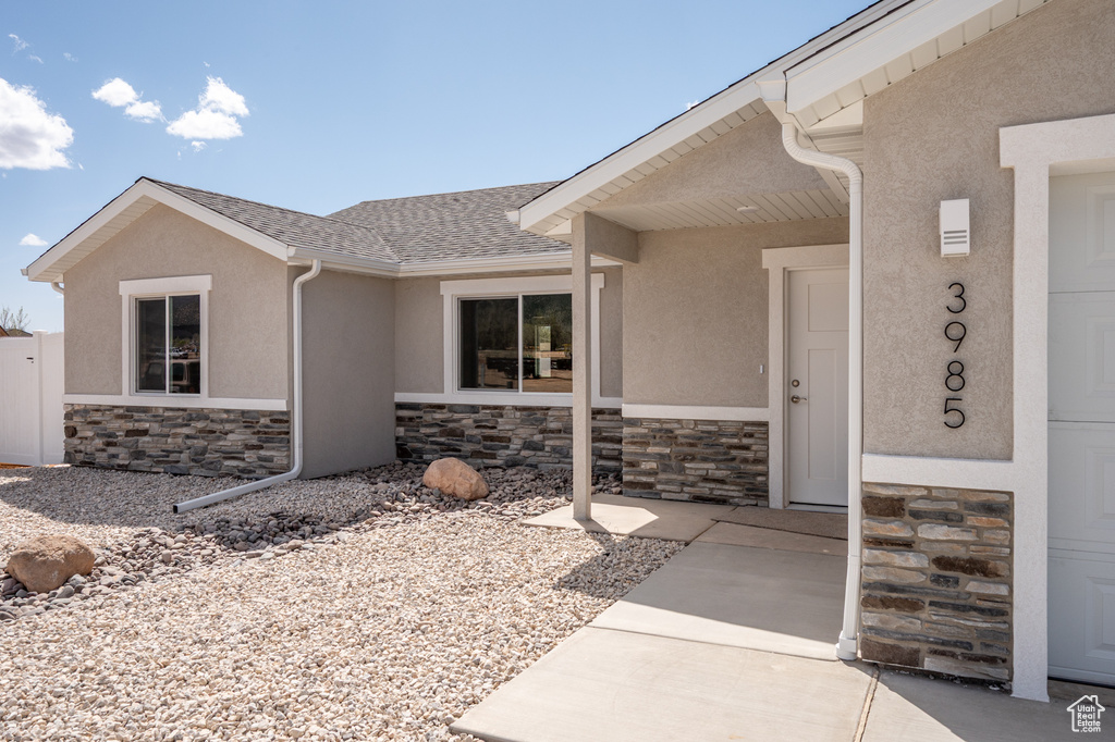 View of exterior entry with a shingled roof, stucco siding, and stone siding