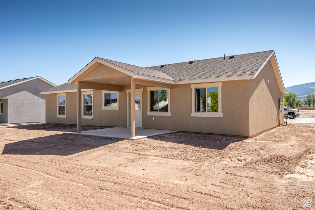 Back of house featuring a patio area, stucco siding, and roof with shingles