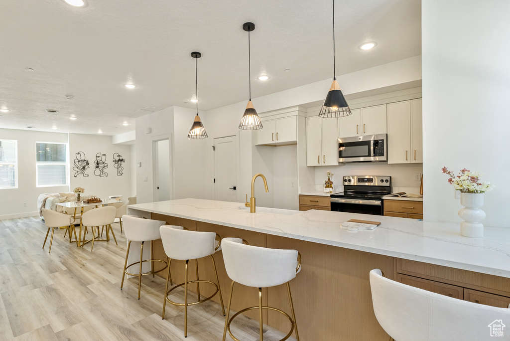 Kitchen featuring a breakfast bar, stainless steel appliances, recessed lighting, light wood-style flooring, and light stone countertops