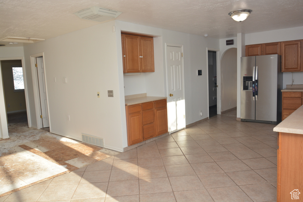 Kitchen featuring visible vents, stainless steel refrigerator with ice dispenser, brown cabinetry, and light tile patterned floors