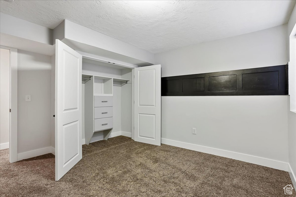 Unfurnished bedroom featuring a textured ceiling, carpet floors, and baseboards