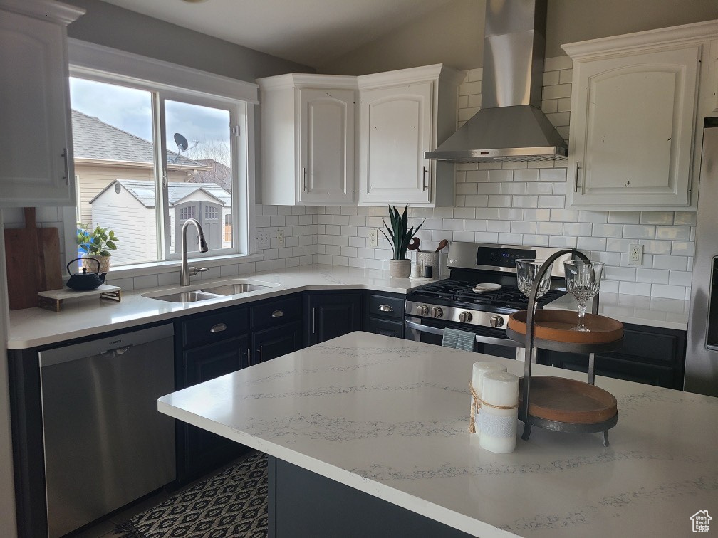Kitchen with stainless steel appliances, decorative backsplash, white cabinetry, a sink, and wall chimney exhaust hood