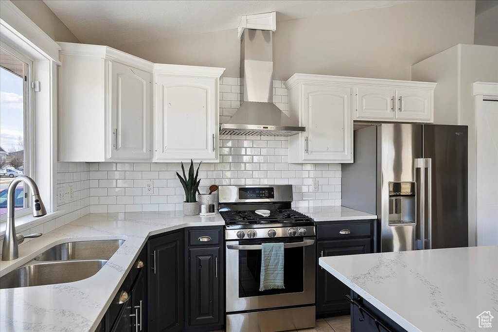 Kitchen with wall chimney exhaust hood, appliances with stainless steel finishes, white cabinets, and a sink